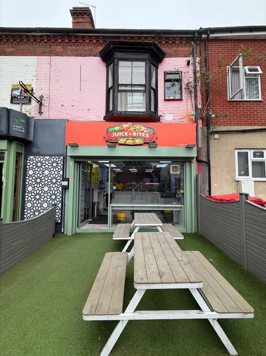 Juice & Bites shopfront on Bristol Road with red sign and outdoor picnic benches